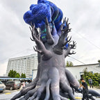 Rear side view of the inflatable tree monster outdoors with people nearby for scale