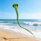 Giant Snake Kite flying above a sandy beach with ocean waves and a clear blue horizon behind it