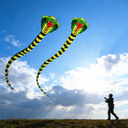 Two Giant Snake Kites flying above a field while a silhouetted person controls the lines at sunset
