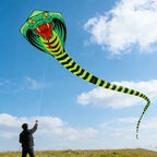 Giant Snake Kite flying over an open field while a person controls the line beneath a bright blue sky