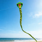 Giant Snake Kite flying high above a sunny beach and ocean with its striped tail curving toward the shore