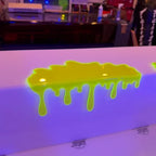 Glowing Slime Shelf Drips — Yellow-green shelf topper resting on a white display edge, viewed from above.