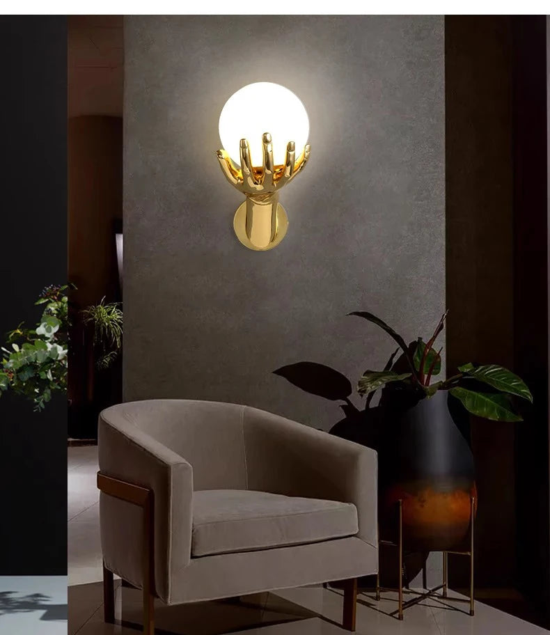 Golden Hand Wall Lamp — Glass shade above a cream armchair beside a large plant