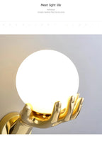 Golden Hand Wall Lamp — Close-up of the illuminated glass globe and gold fingers