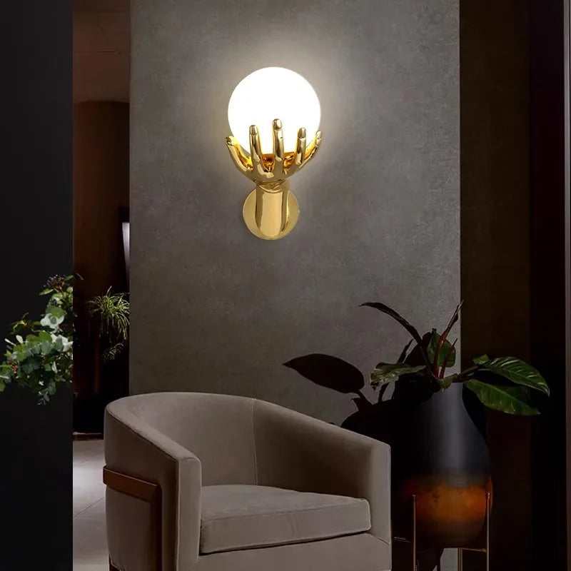 Golden Hand Wall Lamp — Front view of the glass shade above an armchair