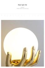 Golden Hand Wall Lamp — Detailed view of the glowing glass globe and polished gold fingers