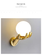 Golden Hand Wall Lamp — Illuminated glass shade and gold hand shown at an angle