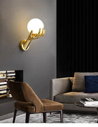 Golden Hand Wall Lamp — Glass shade lighting a living room with a chair and gray sofa