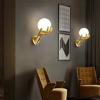 Golden Hand Wall Lamp — Two glass-shade lamps displayed above lounge chairs