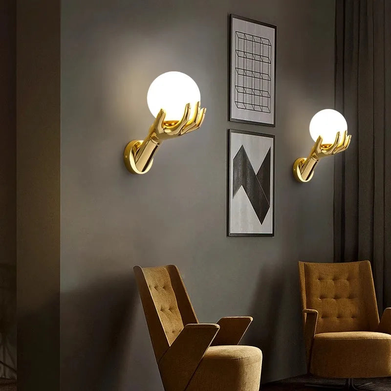 Golden Hand Wall Lamp — Two glass-shade lamps displayed above lounge chairs