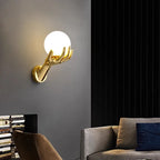 Golden Hand Wall Lamp — Smooth glass shade glowing above a sofa on a dark wall