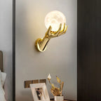 Golden Hand Wall Lamp — Moon shade illuminating a bedside table with a photo frame