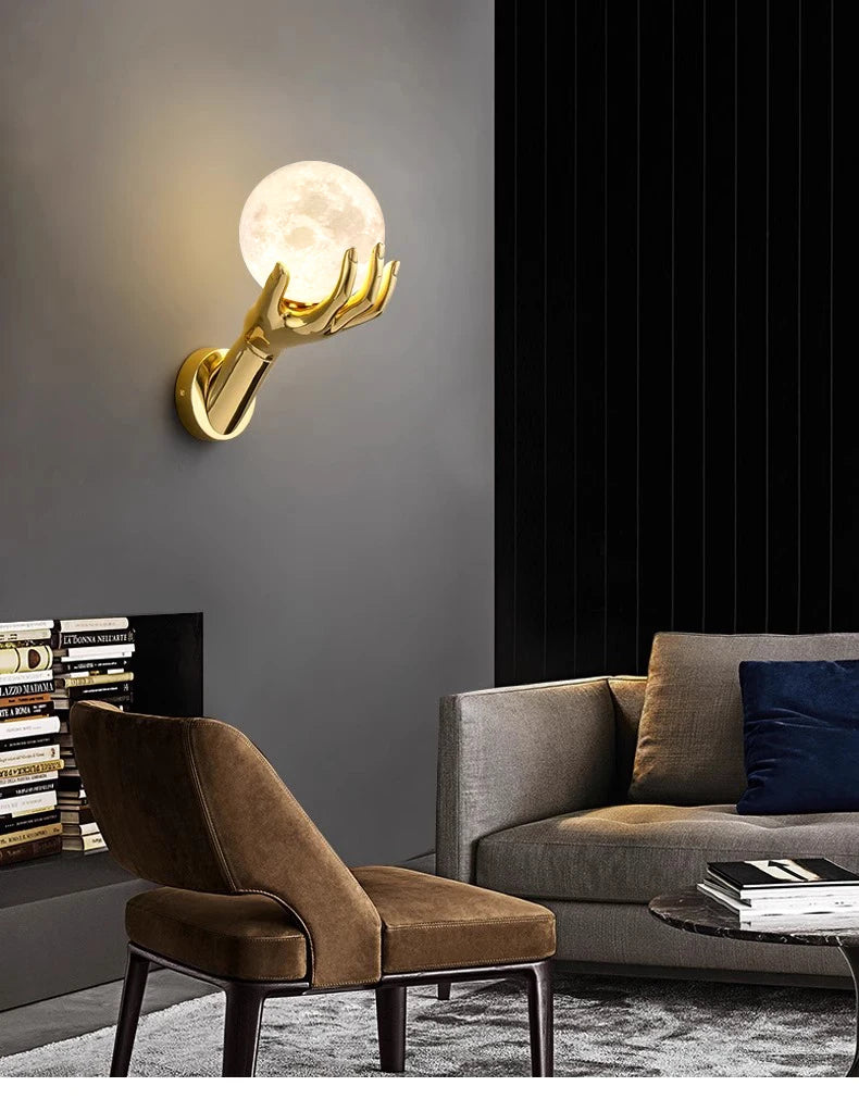 Golden Hand Wall Lamp — Moon shade lighting a living room with a brown chair and gray sofa