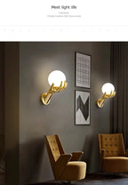 Golden Hand Wall Lamp — Paired glass-shade lamps beside framed artwork in a lounge