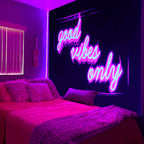 Good Vibes Only Tapestry with pink and blue lettering above a bed in a purple-lit room