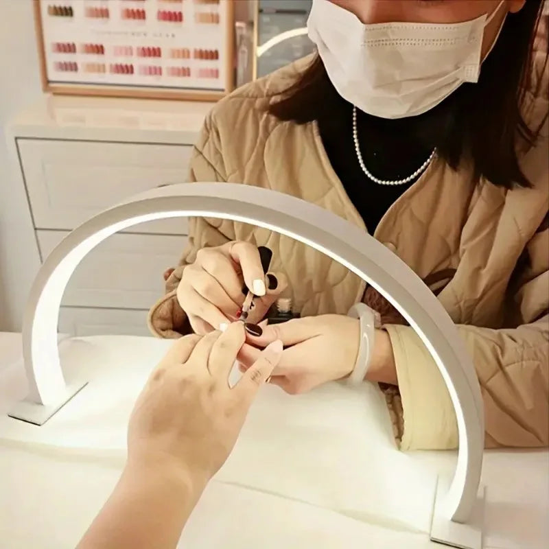 Half Moon Nail Lamp in white lighting a manicure while a nail technician paints a client's nails.