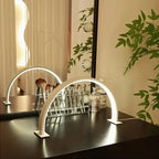 Half Moon Nail Lamp on a black vanity with its illuminated arch reflected in the mirror behind it.