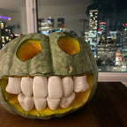 Halloween Pumpkin Teeth Inserts round style forming a full grin in a green pumpkin by a city-view window