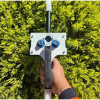 Handheld Wire Puller with black handle held upright outdoors against green foliage.