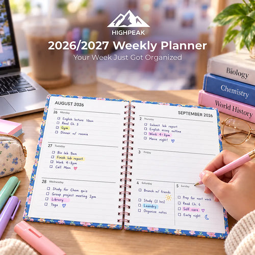 An open spiral-bound 2026/2027 weekly planner shown on a desk with a hand writing in a pink pen. The pages are floral with white writing space and date headers from August 26 to September 3.