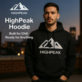 HighPeak Hoodie in black with iconic mountain logo worn by man at dusk, showcasing cozy style and versatile cold-weather wear.