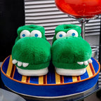 Front view of green crocodile slippers on a blue and yellow striped cushion