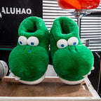 Front-facing crocodile slipper pair displayed on a wooden platform beneath a red stool
