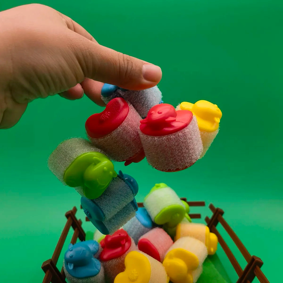 Hand lifting a cluster of colorful attached sheep above the pen