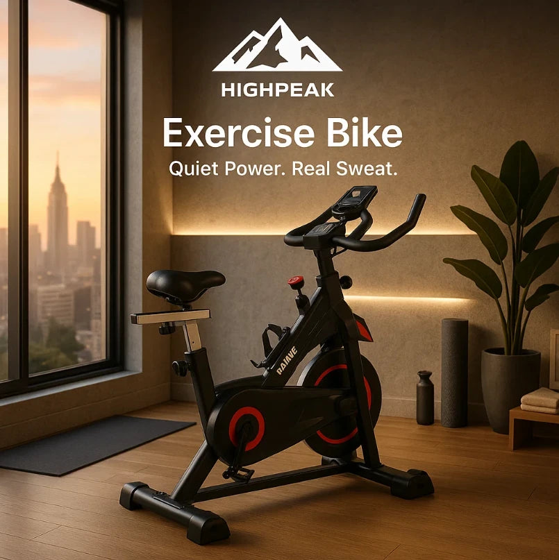 HighPeak Exercise Bike in black with red accents in a modern home gym by a large window at sunset
