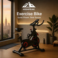 HighPeak Exercise Bike in black with red accents in a modern home gym by a large window at sunset