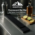 HighPeak Bar Counter Mat in black with fluorescent dots on a stainless steel bar countertop with cocktail tools and sliced citrus.
