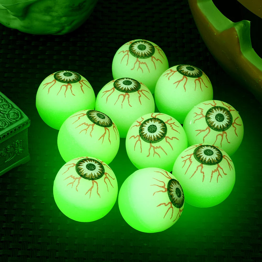 Glowing Eyeball Bouncy Balls with green glow and printed veins on a dark woven surface