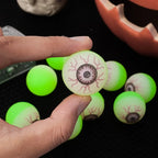 One Glowing Eyeball Bouncy Ball held between two fingers with more balls behind