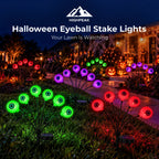 Purple, red and green Halloween eyeball stake lights glowing in a front lawn with pumpkins at night