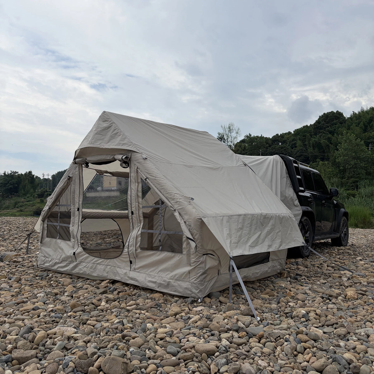 Inflatable Car Camping Tent attached to an SUV on rocky ground, with open doorway and side cover raised