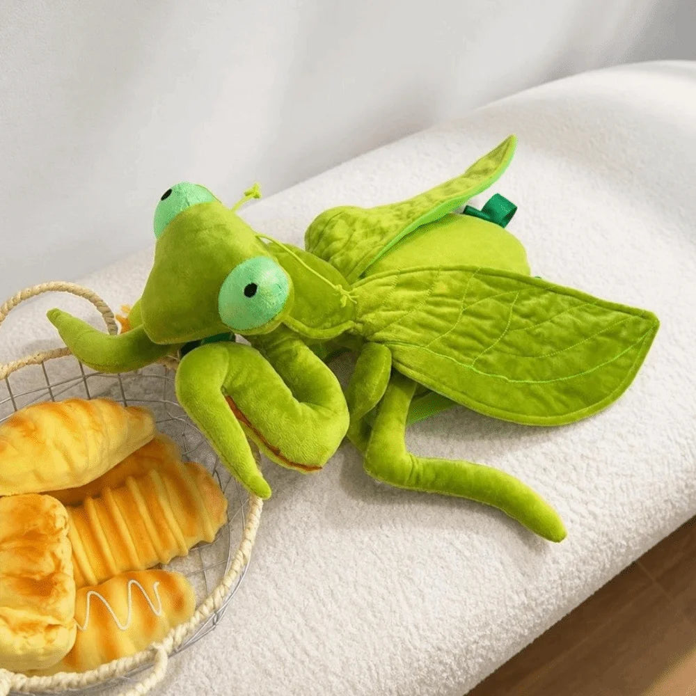 Green Mantis Plush Backpack resting on a bench with leaflike wings spread beside a basket