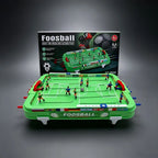 Assembled Mini Foosball Table with green pitch, red goals and retail packaging viewed from the front