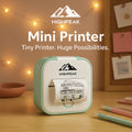 HighPeak Mini Printer in pastel green printing a black and white bus sketch on a wooden desk with warm lighting