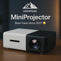HighPeak MiniProjector in black and white on a wood table, compact design with visible lens and ventilation slot.