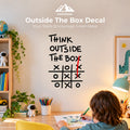 A child drawing at a desk in a bright room, with a large wall decal that reads “THINK OUTSIDE THE BOX” and a tic-tac-toe grid. The scene includes a shelf, plants, pencils, a lamp, and framed wall art.