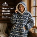 HighPeak Oversized Hoodie Blanket in navy with reindeer pattern and sherpa lining worn by smiling woman by window