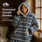 HighPeak Oversized Hoodie Blanket in navy with reindeer pattern and sherpa lining worn by smiling woman by window