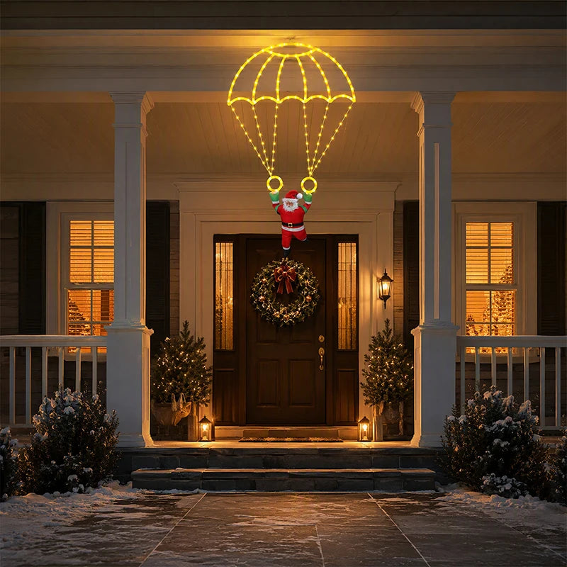 Warm white Parachuting Santa Lights suspended above a wreath-decorated front door on a snowy porch.
