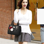 Pebbled Charm Shoulder Purse in black carried with a white sweater and patterned skirt; pom-pom charm shown.
