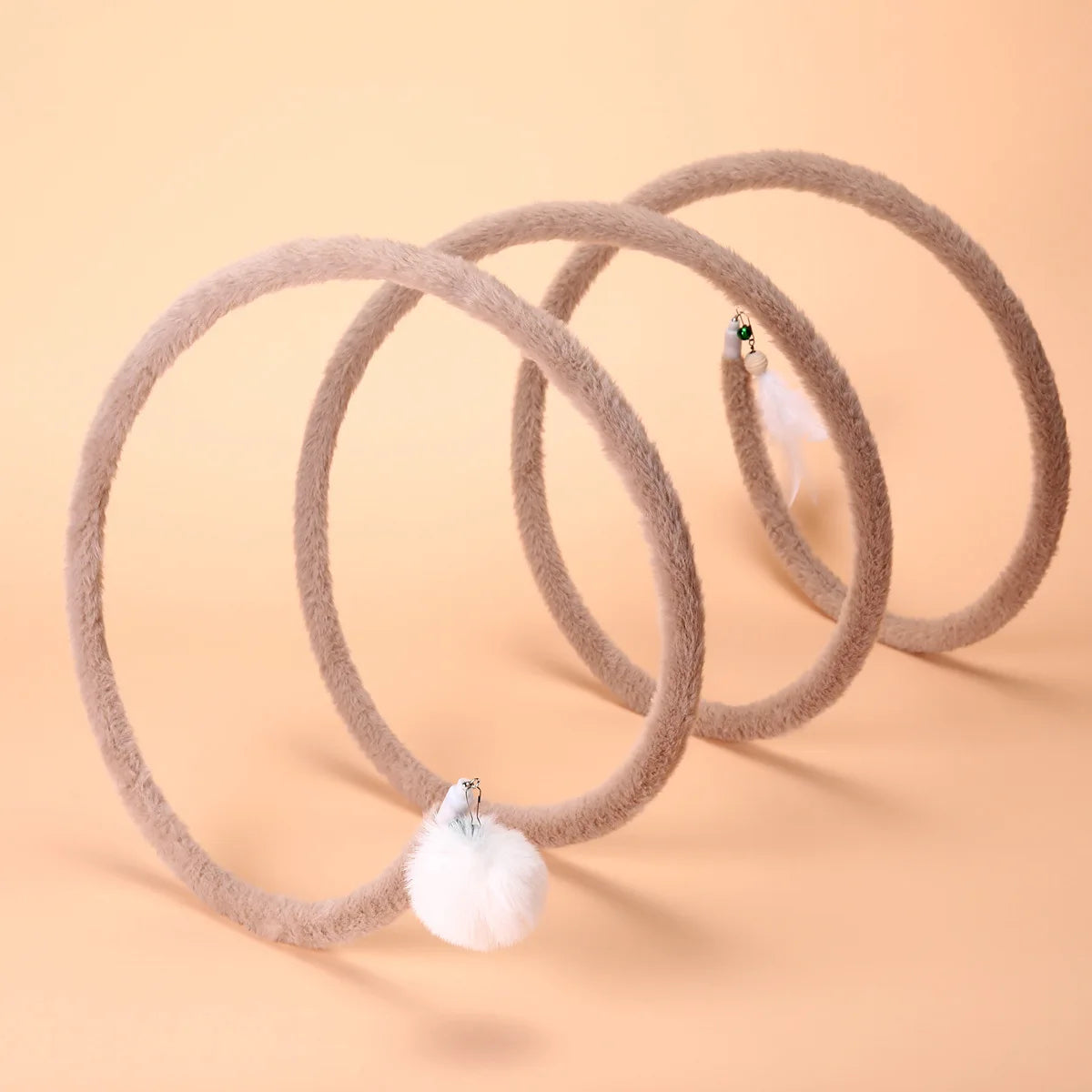 Brown Plush Cat Spiral Toy with pom-pom and feather attachments on a peach background