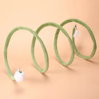 Green Plush Cat Spiral Toy with white pom-pom and feather attachments on a peach background
