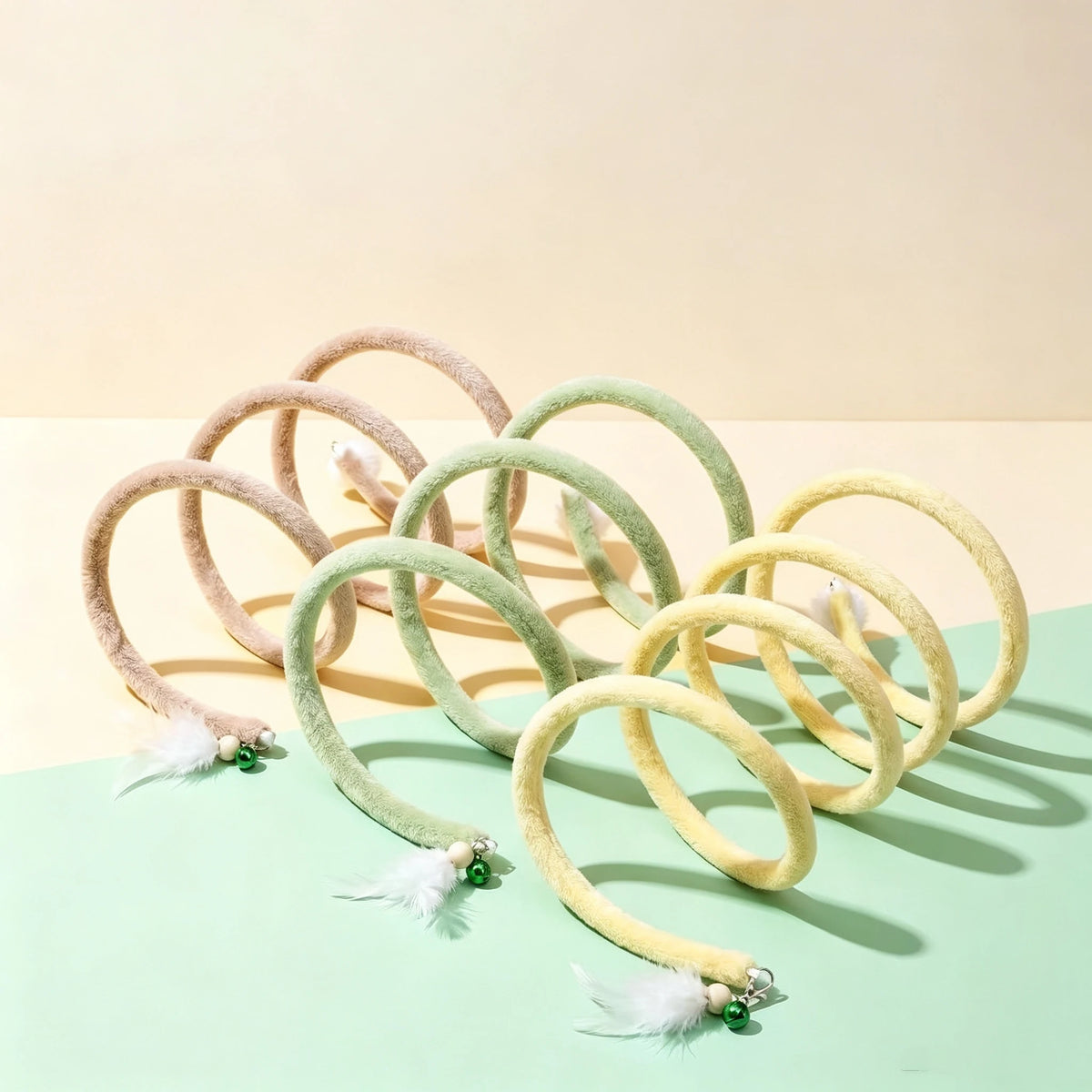 Brown, green and yellow Plush Cat Spiral Toys displayed on a pastel green and yellow background