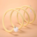 Yellow Plush Cat Spiral Toy with white pom-pom and feather attachments on a peach background