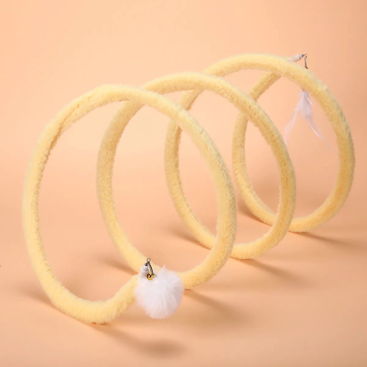 Yellow Plush Cat Spiral Toy with white pom-pom and feather attachments on a peach background