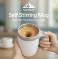 HighPeak Self Stirring Mug in gray and white held in hands with coffee mixing inside, kitchen background visible